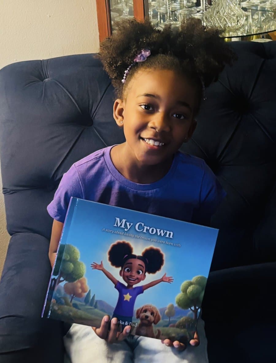 Emeka smiling on the couch, holding her hardcover copy of My Crown